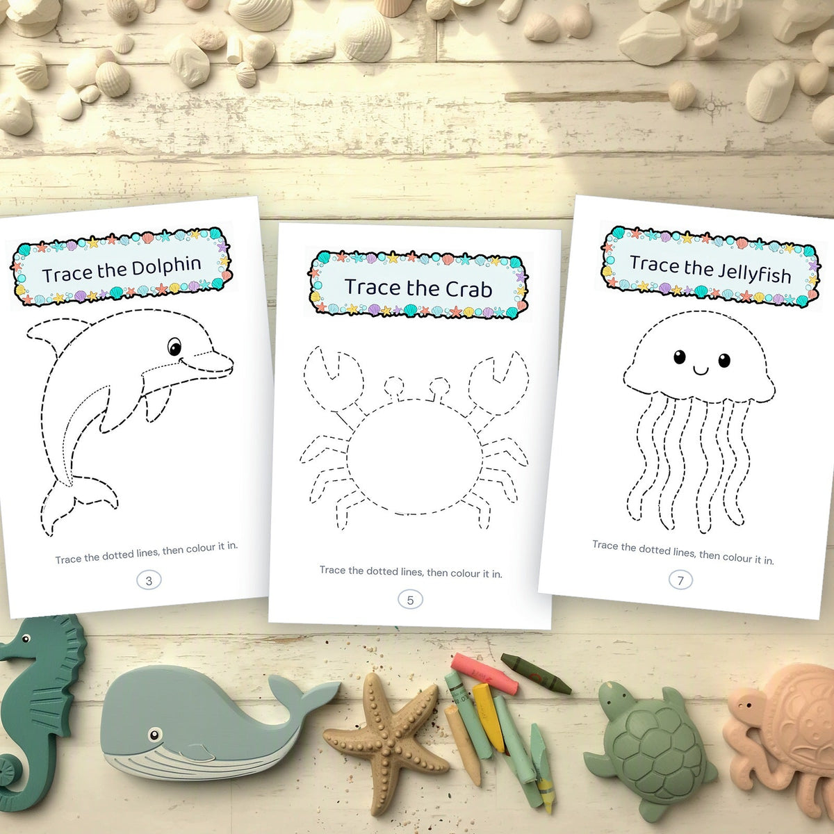 Three printed tracing pages - dolphin, crab and jellyfish - beside wooden sea animal toys